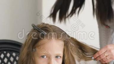 不开心的小女孩。 妈妈或理发师给她的辫子编辫子。 棕色头发